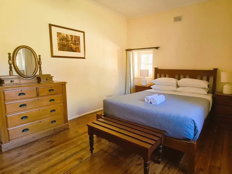 A queen bed sits in a large bedroom with wooden floorboards